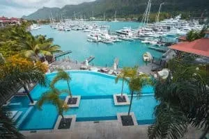 Infinity pool with palm trees overlooking yachts docked at a Eden Island marina surrounded by lush hills in Seychelles.