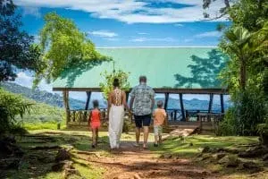 A family walking toward a green-roofed pavilion overlooking mountain vistas and lush landscapes in Seychelles.
