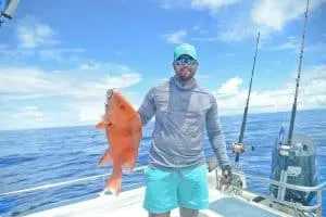 A fisherman proudly displaying a bright red snapper caught during a deep-sea fishing trip in Seychelles' azure waters.