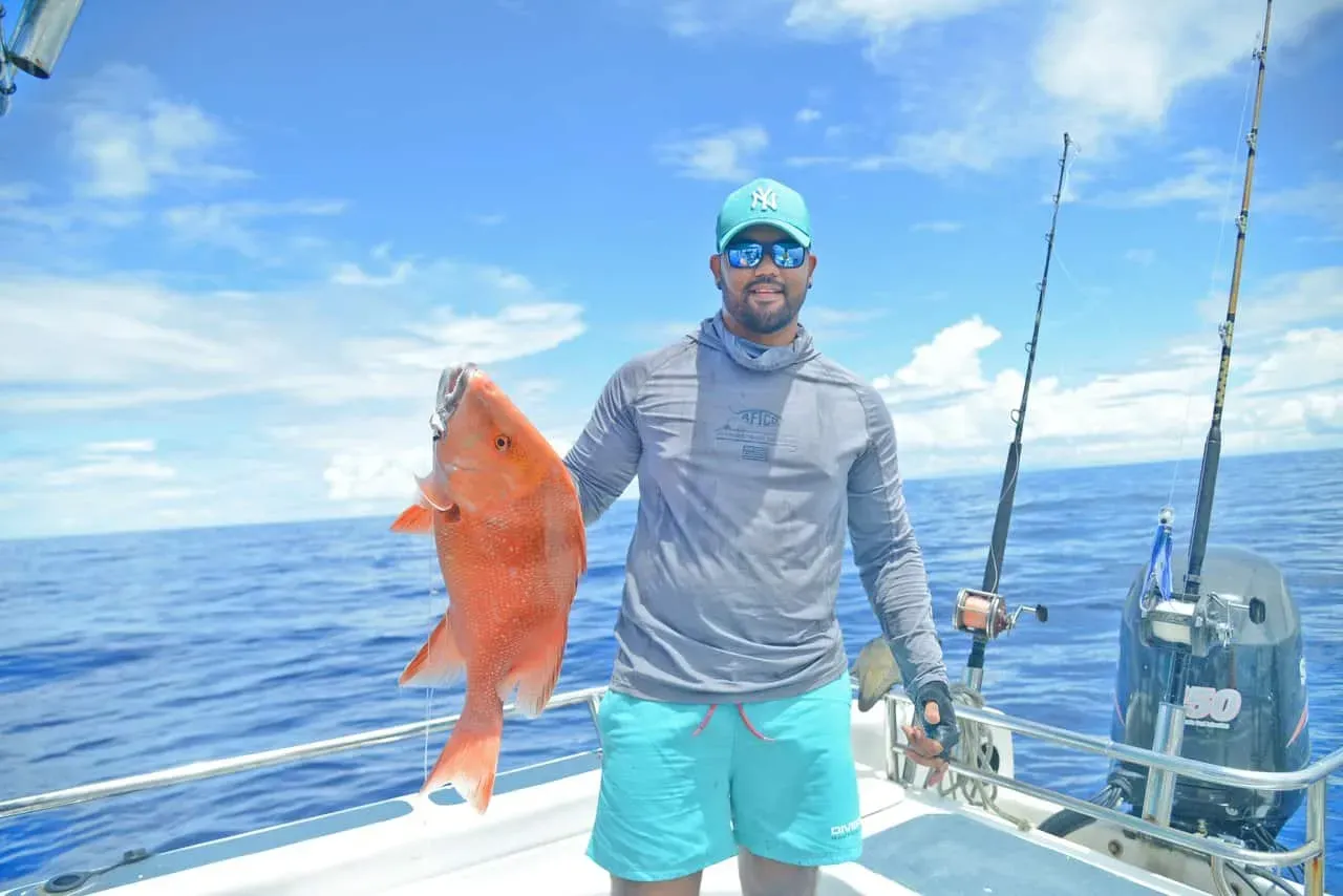 A fisherman proudly displaying a bright red snapper caught during a deep-sea fishing trip in Seychelles' azure waters.