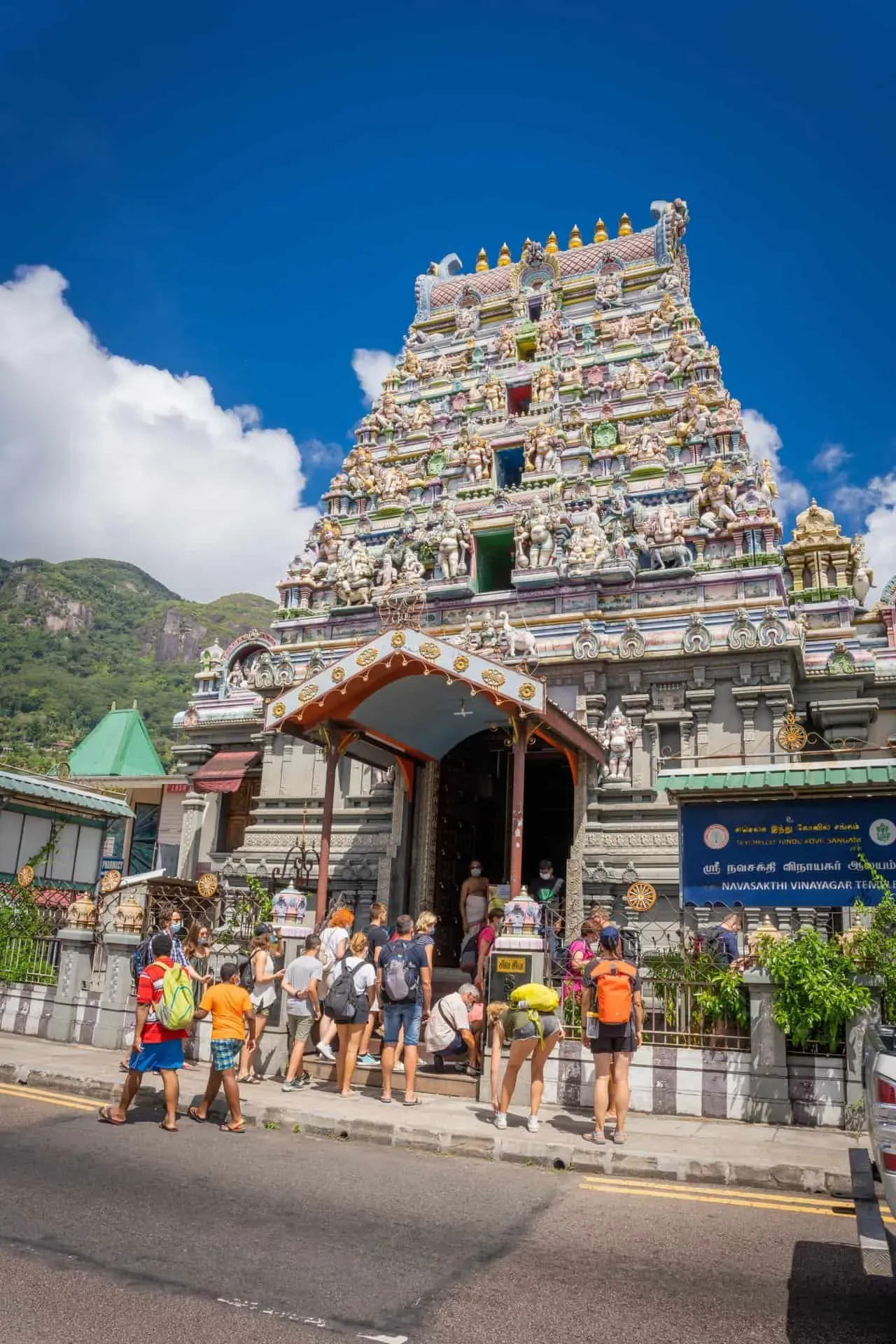 Colorful exterior of the Arulmigu Navasakti Vinayagar Hindu temple in Victoria, Seychelles, with tourists gathered at the entrance under clear blue sky.