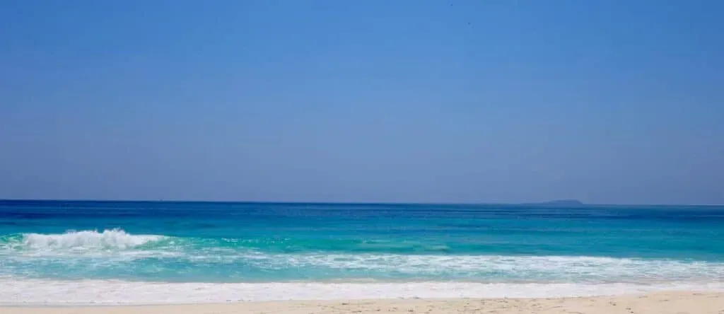 Pristine sandy beach with turquoise waves under a clear blue sky in Seychelles.